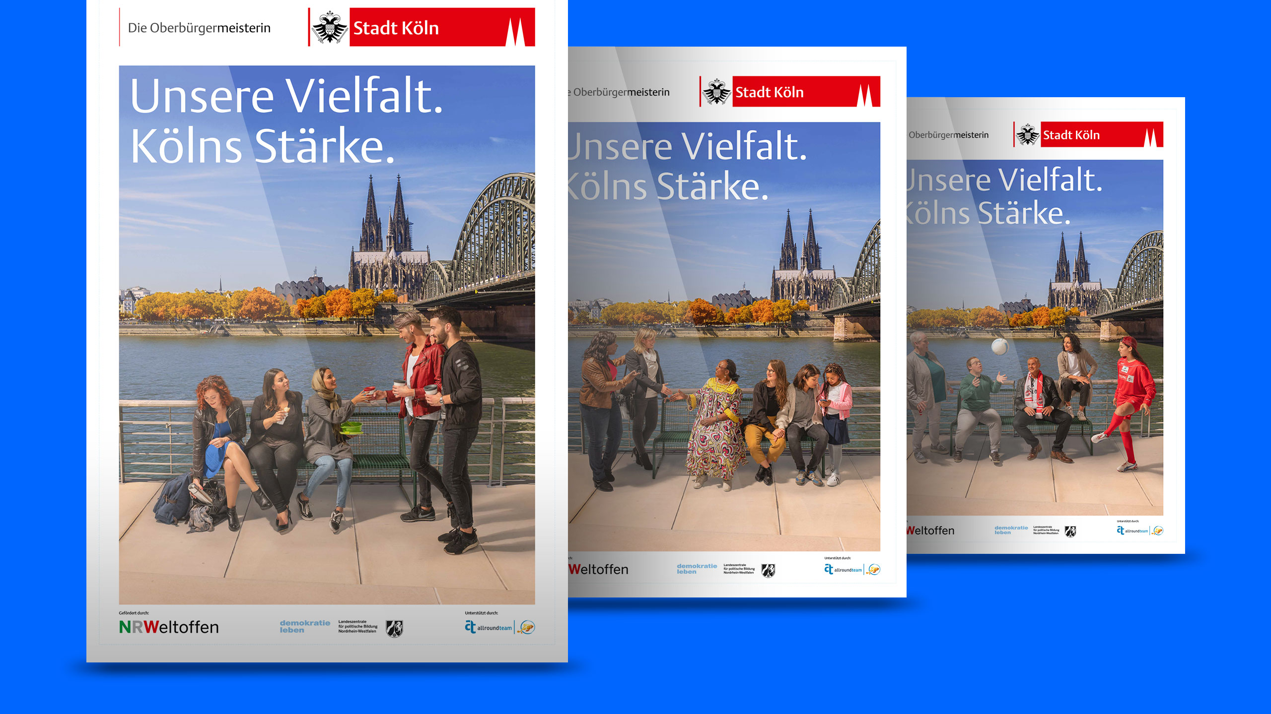 Das Bild zeigt drei großformatige Plakate nebeneinander, jeweils vor der ikonischen Kulisse des Kölner Doms und der Hohenzollernbrücke. Die Szene wirkt herbstlich, mit farbigen Bäumen im Hintergrund. Auf jedem Plakat sitzen oder stehen unterschiedliche Gruppen von Menschen an der Rheinpromenade – sie unterhalten sich, begegnen sich oder genießen die Umgebung. Die Personen repräsentieren verschiedene Altersgruppen, Hintergründe und Lebensrealitäten. Alle Plakate tragen oben ein rot‑weißes Banner mit dem Stadt‑Köln‑Logo und den Worten „Die Oberbürgermeisterin“ sowie den zentralen Kampagnenclaim „Unsere Vielfalt. Kölns Stärke.“. Am unteren Rand befinden sich Logos unterstützender Organisationen. Die Gesamtwirkung vermittelt ein starkes Bild von Diversität, Zusammenhalt und gelebter Vielfalt im öffentlichen Raum.